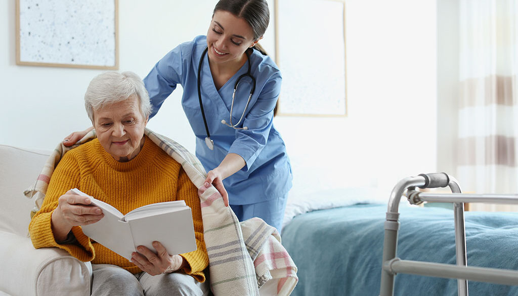 A Hospice Nurse Putting A Blanket Over A Hospice Patient Sitting In A Chair Reading A Book Benefits Of Hospice Care Donations