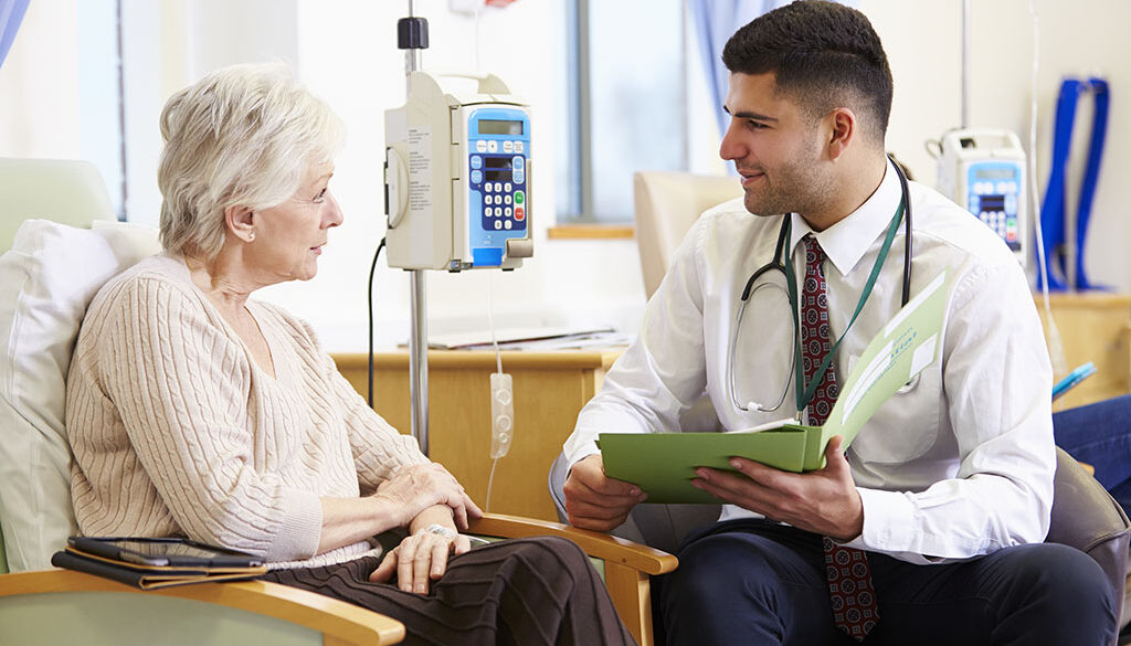 A Doctor Sitting Beside A Senior Woman Receiving Curative Treatment In Palliative Care Discussing Care Options