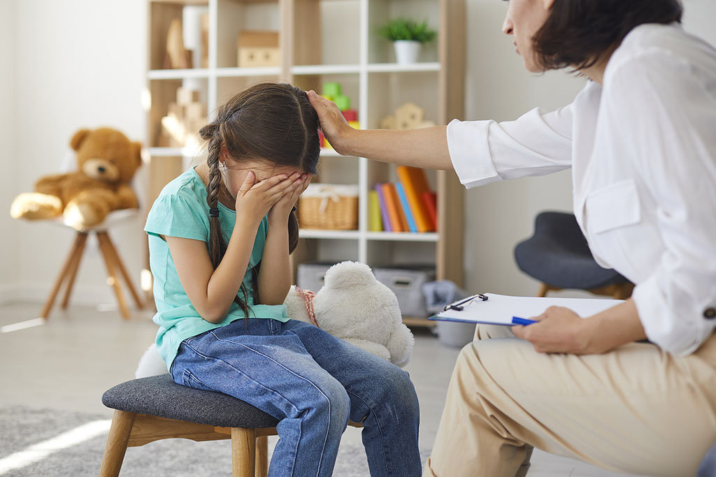 importance-of-children-grief-counseling A Therapist Counseling A Young Girl Sitting On A Stool With Her Hands Covering Her Face Grief Counseling For Children